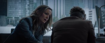 Movie still from “Blacklight” (2022), directed by Mark Williams – A woman sitting in front of a window with her mouth wide open; Medium shot, Over the shoulder angle