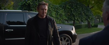 Movie still from “Blacklight” (2022), directed by Mark Williams – A man in a black jacket standing in front of a car; Medium shot, Over the shoulder angle