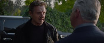 Movie still from “Blacklight” (2022), directed by Mark Williams – A man wearing a black jacket talking to another man; Close Up shot, Over the shoulder angle