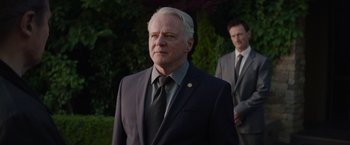 Movie still from “Blacklight” (2022), directed by Mark Williams – A man in a suit and tie standing next to another man; Close Up shot, Low angle