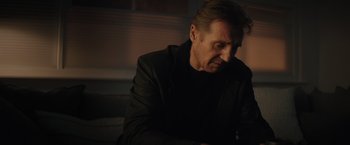 Movie still from “Blacklight” (2022), directed by Mark Williams – A man in a black jacket sitting on a bench; Close Up shot, Low angle