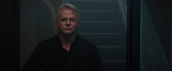 Movie still from “Blacklight” (2022), directed by Mark Williams – A man in a black shirt standing in front of a staircase; Close Up shot, Low angle