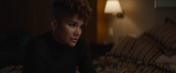 Movie still from “Blacklight” (2022), directed by Mark Williams – A woman sitting on a bed in a room with a lamp; Close Up shot, Low angle