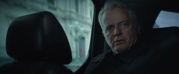 Movie still from “Blacklight” (2022), directed by Mark Williams – An older man sitting in the passenger seat of a car; Close Up shot, Over the shoulder angle