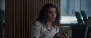 Movie still from “Blacklight” (2022), directed by Mark Williams – A woman with curly hair is holding a tablet; Close Up shot, Over the shoulder angle