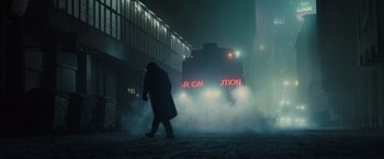 Movie still from “Blade Runner 2049” (2017), directed by Denis Villeneuve – A person walking on a street with a train in the background; Extreme Wide shot, Low angle