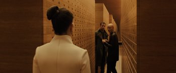 Movie still from “Blade Runner 2049” (2017), directed by Denis Villeneuve – Two men and a woman are standing in a hallway; Wide shot, Over the shoulder angle