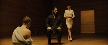 Movie still from “Blade Runner 2049” (2017), directed by Denis Villeneuve – A man sitting on top of a chair next to a woman; Medium shot, Low angle