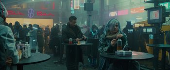 Movie still from “Blade Runner 2049” (2017), directed by Denis Villeneuve – A man and a woman sitting at tables in a restaurant; Wide shot, Over the shoulder angle