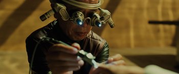 Movie still from “Blade Runner 2049” (2017), directed by Denis Villeneuve – An older man wearing a pair of glasses and a helmet; Close Up shot, Over the shoulder angle