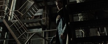 Movie still from “Blade Runner 2049” (2017), directed by Denis Villeneuve – A man holding a gun while standing next to a building; Medium shot, Low angle