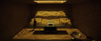 Movie still from “Blade Runner 2049” (2017), directed by Denis Villeneuve – A woman standing in front of a desk in a dimly - lit room; Extreme Wide shot, High angle