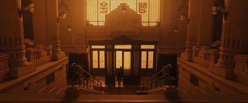 Movie still from “Blade Runner 2049” (2017), directed by Denis Villeneuve – A person standing in front of a building with a clock on it's wall; Extreme Wide shot, Low angle