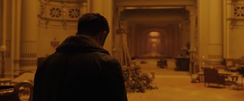 Movie still from “Blade Runner 2049” (2017), directed by Denis Villeneuve – A man standing in front of an open fire place; Wide shot, Over the shoulder angle
