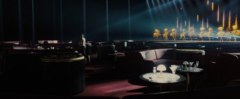 Movie still from “Blade Runner 2049” (2017), directed by Denis Villeneuve – A room filled with couches and a table in front of a stage; Extreme Wide shot, High angle