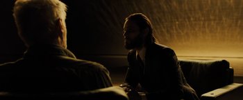 Movie still from “Blade Runner 2049” (2017), directed by Denis Villeneuve – A man in a suit is sitting in a dimly - lit room; Medium shot, Over the shoulder angle