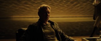 Movie still from “Blade Runner 2049” (2017), directed by Denis Villeneuve – An older man sitting on a couch in a dark room; Close Up shot, Low angle