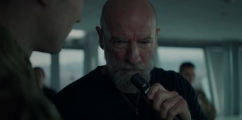 Movie still from “Blood Red Sky” (2021), directed by Peter Thorwarth – An older man with a beard is holding a microphone in his mouth; Close Up shot, Over the shoulder angle