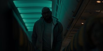 Movie still from “Blood Red Sky” (2021), directed by Peter Thorwarth – A man standing in a dark room with a light shining on him; Medium shot, Low angle