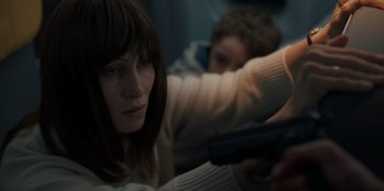 Movie still from “Blood Red Sky” (2021), directed by Peter Thorwarth – A woman sitting in front of a man holding a gun; Close Up shot, High angle