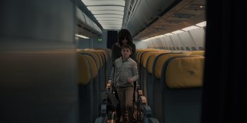 Movie still from “Blood Red Sky” (2021), directed by Peter Thorwarth – A woman and a child are walking down the aisle of an airplane; Wide shot, Low angle