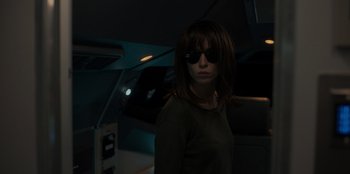 Movie still from “Blood Red Sky” (2021), directed by Peter Thorwarth – A woman wearing sunglasses standing in a dark room; Medium shot, Low angle