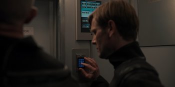 Movie still from “Blood Red Sky” (2021), directed by Peter Thorwarth – A man holding a cell phone in front of a wall; Close Up shot, Over the shoulder angle