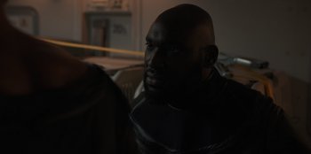 Movie still from “Blood Red Sky” (2021), directed by Peter Thorwarth – A man with a bald head is sitting in a room; Close Up shot, Over the shoulder angle