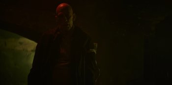 Movie still from “Blood Red Sky” (2021), directed by Peter Thorwarth – A man with a bald head standing in a dark room; Medium shot, Low angle