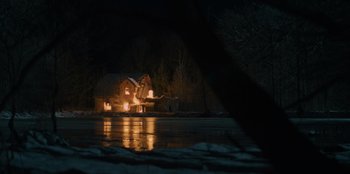 Movie still from “Blood Red Sky” (2021), directed by Peter Thorwarth – A house is lit up at night on the water; Extreme Wide shot, Low angle
