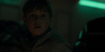 Movie still from “Blood Red Sky” (2021), directed by Peter Thorwarth – A young boy in a dark room with a light in the background; Close Up shot, Over the shoulder angle