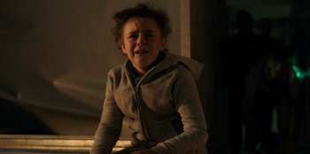 Movie still from “Blood Red Sky” (2021), directed by Peter Thorwarth – A young boy is sitting in a dark room; Medium shot, Low angle