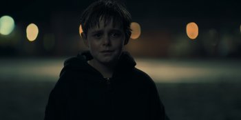 Movie still from “Blood Red Sky” (2021), directed by Peter Thorwarth – A boy in a black jacket is standing in the dark; Close Up shot, Over the shoulder angle