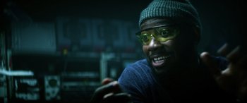 Movie still from “Bloodshot” (2020), directed by Dave Wilson – A man wearing glasses and a hat is smiling for the camera; Close Up shot, Over the shoulder angle
