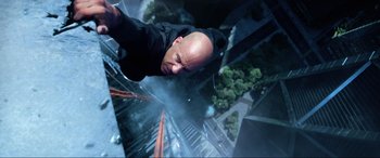 Movie still from “Bloodshot” (2020), directed by Dave Wilson – A bald man hanging from the side of a tall building; Close Up shot, Overhead angle