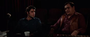 Movie still from “Blow Out” (1981), directed by Brian De Palma – Two people sitting at a table in front of each other in a movie theater; Medium shot, Over the shoulder angle