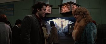 Movie still from “Blow Out” (1981), directed by Brian De Palma – A man in a suit is talking to a woman in front of a train station; Medium shot, Over the shoulder angle