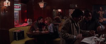 Movie still from “Blow Out” (1981), directed by Brian De Palma – A man and a woman sitting at a table in a restaurant; Wide shot, Over the shoulder angle