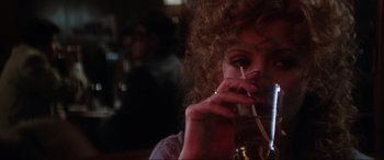 Movie still from “Blow Out” (1981), directed by Brian De Palma – A woman sitting at a table with a drink in her hand; Close Up shot, Over the shoulder angle