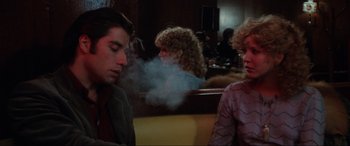 Movie still from “Blow Out” (1981), directed by Brian De Palma – A man and a woman sitting at a table in front of each other; Medium shot, Over the shoulder angle
