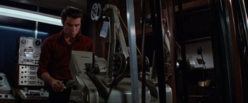Movie still from “Blow Out” (1981), directed by Brian De Palma – A man in a red shirt working on a laptop; Medium shot, Low angle