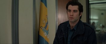 Movie still from “Blow Out” (1981), directed by Brian De Palma – A man in front of a flag in a room; Close Up shot, Over the shoulder angle