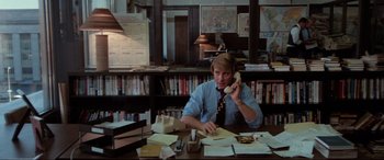 Movie still from “Blow Out” (1981), directed by Brian De Palma – A man sitting at a desk talking on a phone; Medium shot, High angle
