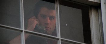 Movie still from “Blow Out” (1981), directed by Brian De Palma – A man is talking on a cell phone through a window; Close Up shot, Low angle