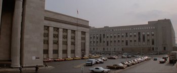 Movie still from “Blow Out” (1981), directed by Brian De Palma – Cars are parked in a parking lot in front of a large building; Extreme Wide shot, Low angle
