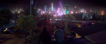 Movie still from “Blue Beetle” (2023), directed by Angel Manuel Soto – Two people sitting on a bench in front of a city at night; Extreme Wide shot, High angle