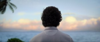Movie still from “Blue Beetle” (2023), directed by Angel Manuel Soto – A man with curly hair is looking out at the ocean; Close Up shot, Low angle