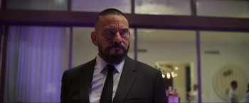 Movie still from “Blue Beetle” (2023), directed by Angel Manuel Soto – A man in a black suit and a black tie; Close Up shot, Over the shoulder angle