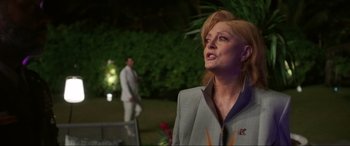 Movie still from “Blue Beetle” (2023), directed by Angel Manuel Soto – An older woman in a gray suit looking up at the sky; Close Up shot, Over the shoulder angle