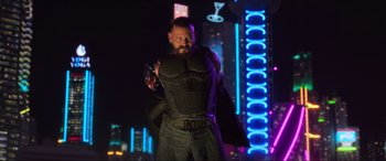 Movie still from “Blue Beetle” (2023), directed by Angel Manuel Soto – A man with a gun in his hand in front of neon lights; Medium shot, Low angle